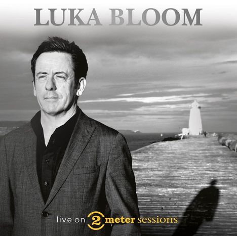 "LUKA BLOOM, live on 2 meter sessions" steht geschrieben. Ein Mann im Anzug steht vor einem Steg mit einem Leuchtturm.