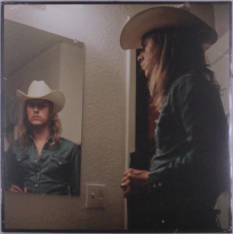 Ich sehe keine Texte. Ein Mann mit Cowboyhut steht vor einem Spiegel. Sein Spiegelbild zeigt ihn frontal.