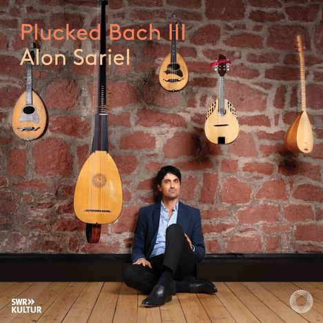 "Plucked Bach III, Alon Sariel." Mann in Anzug sitzt vor roter Steinwand, umgeben von Saiteninstrumenten.