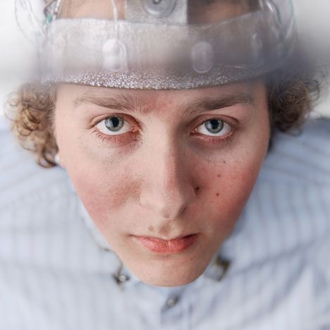 Ein Mensch mit lockigem Haar trägt ein futuristisches Stirnband mit Drähten und schaut direkt nach vorne.