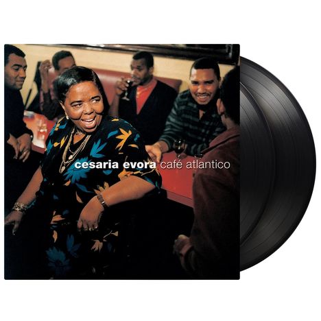 "cesaria evora café atlantico"; eine Frau in bunter Kleidung lacht mit mehreren Personen an einem Tisch. Vinyl im Hintergrund.
