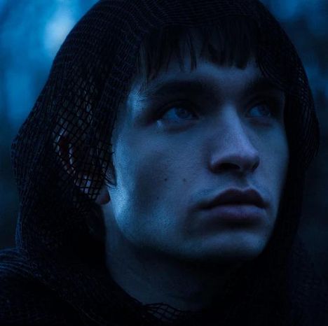 Eine Person mit einem schwarzen Netzschal schaut nachdenklich nach oben, in tiefblauem Licht getaucht.