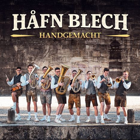 Text: "HÅFN BLECH HANDGEMACHT". Eine Gruppe Männer in traditioneller Kleidung mit Blasinstrumenten vor einer Steinmauer.