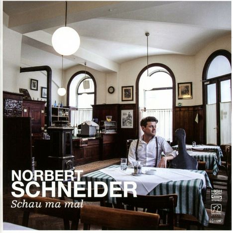 Text: "Norbert Schneider, Schau ma mal." Ein Mann sitzt in einem traditionellen Kaffeehaus mit Holzmöbeln und Tischdecken.