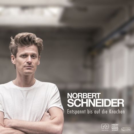 Norbert Schneider, Entspannt bis auf die Knochen. Mann in weißem Shirt, Arme verschränkt, verschwommener Hintergrund.