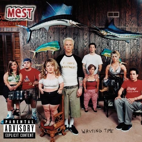 Große Buchstaben "MEST" und "WASTING TIME". Menschen in einem Raum mit Holzvertäfelung und zwei großen Fischen an der Wand.