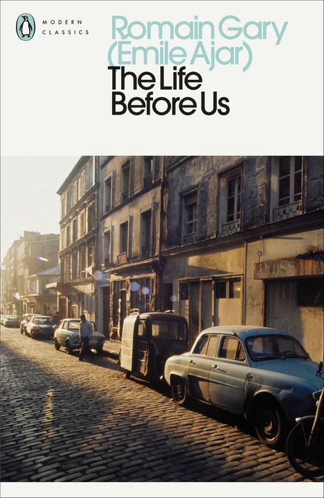 "Romain Gary (Emile Ajar), The Life Before Us." Eine sonnige Straße mit alten Autos und Gebäuden. Vintage-Stimmung.