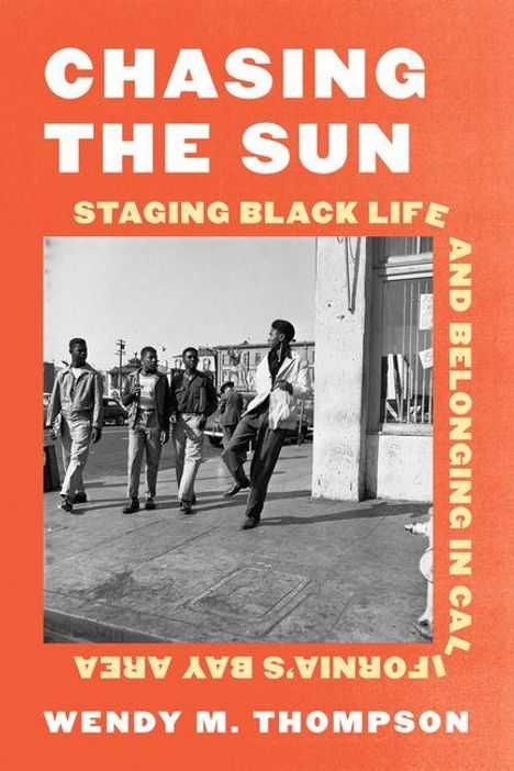 CHASING THE SUN. Fünf Männer stehen locker auf einem Gehweg vor Geschäften. Orange Hintergrund mit weißem Text.