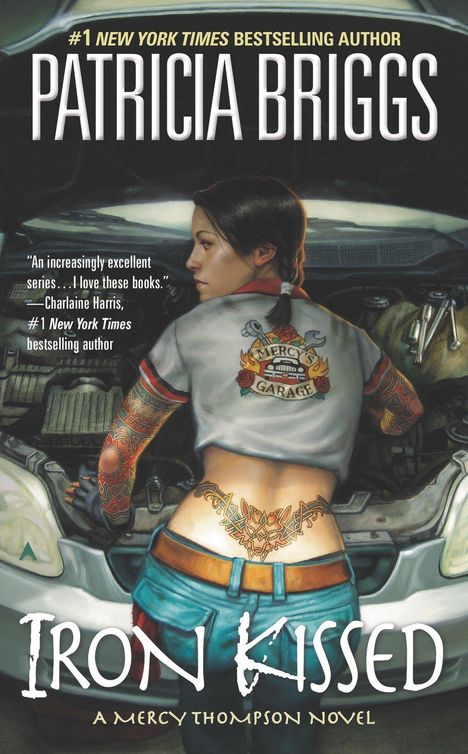 „#1 New York Times Bestselling Author Patricia Briggs“, „Mercy's Garage“ auf dem Rücken einer Frau beim Auto reparieren.