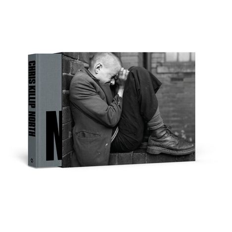 CHRIS KILLIP NORTH. Ein sitzender Mann lehnt sich verzweifelt gegen die Mauer, seine Kleidung ist schlicht und seine Haltung gekrümmt.