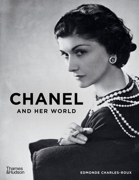 "CHANEL AND HER WORLD" in schwarzer Schrift. Schwarz-weißes Porträt einer Frau mit Perlenkette und Ohrringen.