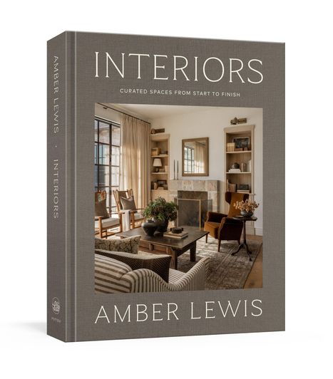 "INTERIORS" und "AMBER LEWIS" sind prominent sichtbar. Ein einladender Wohnraum mit Sofa, Kamin und Regalen.