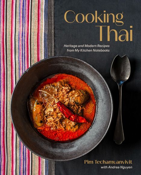 "Cooking Thai" steht in goldener Schrift; darunter ein schwarzer Teller mit rotem Curry und Chilischote auf gestreiftem Tuch.
