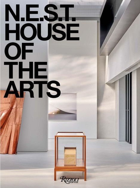 N.E.S.T. HOUSE OF THE ARTS in großen schwarzen Buchstaben. Moderne Innenarchitektur mit Kunstwerk und Holztisch.