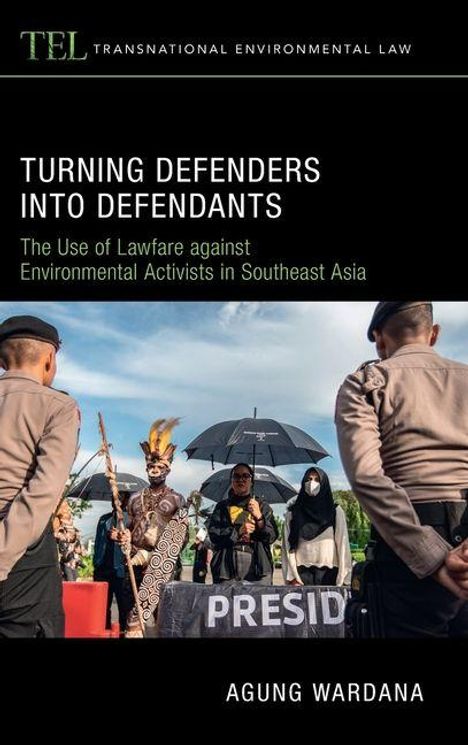 „Turning Defenders into Defendants“: Personen in traditioneller Kleidung und Uniformen, Regenschirme im Hintergrund.