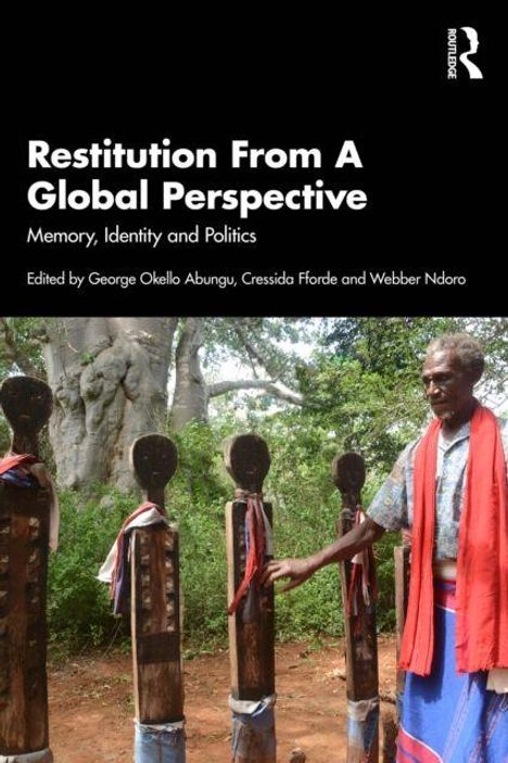 „Restitution From A Global Perspective: Memory, Identity and Politics.“ Mann berührt Statuen, Bäume im Hintergrund.