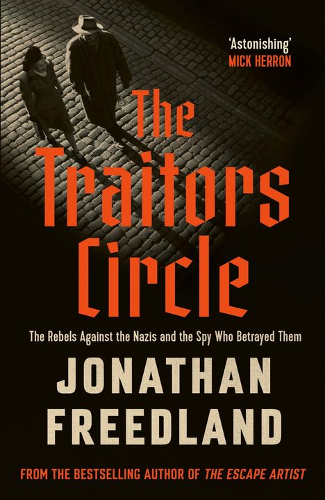 „The Traitors Circle“ von Jonathan Freedland. Zwei Personen gehen auf Kopfsteinpflaster im Schatten.
