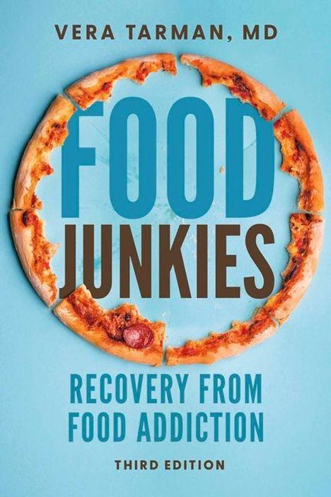 "FOOD JUNKIES" steht in großen Buchstaben. Ein Pizzastück fehlt aus einer ganzen Pizza; blauer Hintergrund.