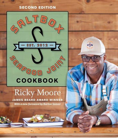 "Saltbox Seafood Joint Cookbook", "Second Edition", "Ricky Moore", "James Beard Award Winner". Ein Mann lächelt, Holzhintergrund.