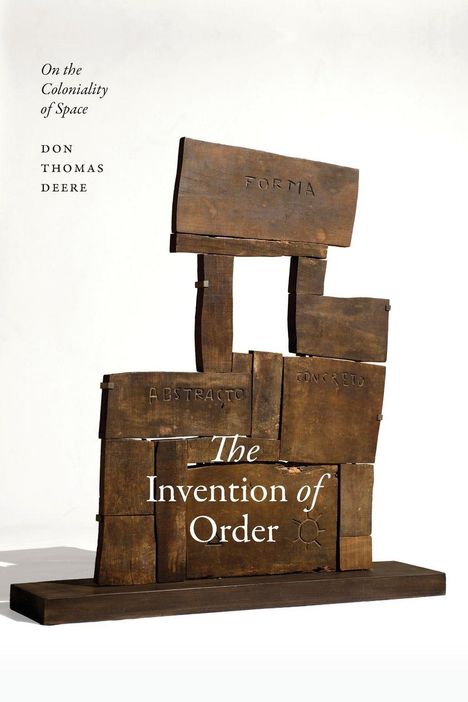 Text: "On the Coloniality of Space, Don Thomas Deere, The Invention of Order." Eine Skulptur aus Holz mit eingravierten Wörtern.