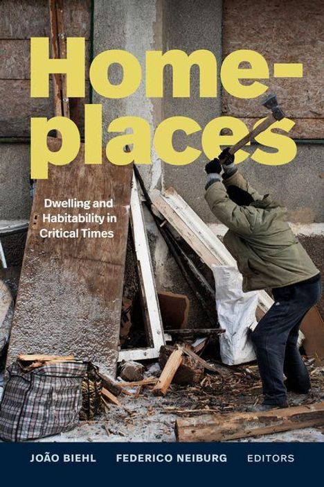 „Home-places: Dwelling and Habitability in Critical Times“. Ein Mann zerschlägt mit einem Vorschlaghammer Holz vor einem Gebäude.