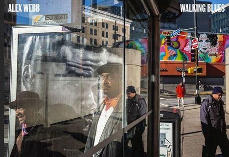 ALEX WEBB, WALKING BLUES: Reflexion einer Person in Schaufenster, Hintergrund mit buntem Wandbild, Straßenszene.