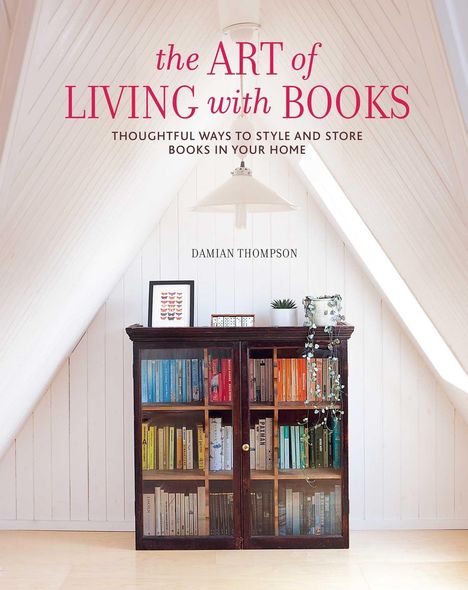 Text im Bild: "the ART of LIVING with BOOKS. THOUGHTFUL WAYS TO STYLE AND STORE BOOKS IN YOUR HOME. DAMIAN THOMPSON." Holzregal in Dachgeschoss mit bunten Büchern.