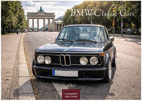 Aufschrift: "BMW Classic Cars". Historisches Auto vor dem Brandenburger Tor, Straße gesäumt von Bäumen.