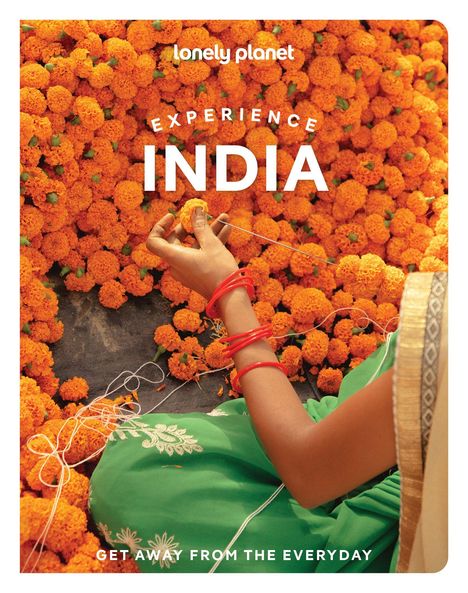 „Experience India. Get away from the everyday.“ Eine Person fädelt orangefarbene Blüten inmitten eines Blütenmeers auf.