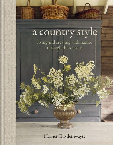 „a country style: living and creating with nature“. Ein rustikaler Schrank, darauf Körbe, unten ein Blumenarrangement.