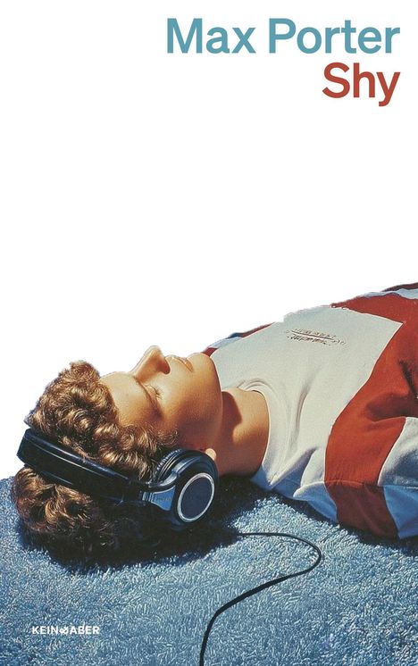 Text: "Max Porter Shy". Ein Junge mit Kopfhörern liegt auf einem blauen Teppich.