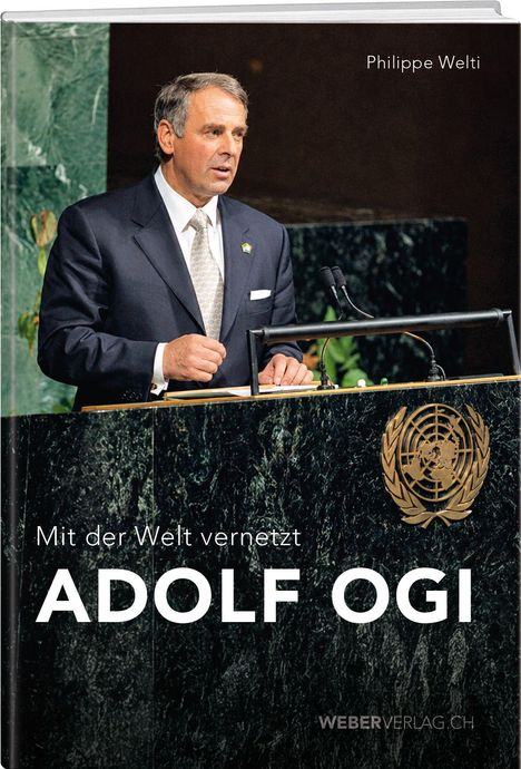 "Mit der Welt vernetzt ADOLF OGI" steht unten. Oben "Philippe Welti". Ein Mann am Rednerpult der Vereinten Nationen.