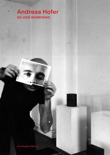 "Andreas Hofer, so und anderswo." Eine Person hält ein Foto vor das Gesicht, in einem minimalistisch eingerichteten Raum.