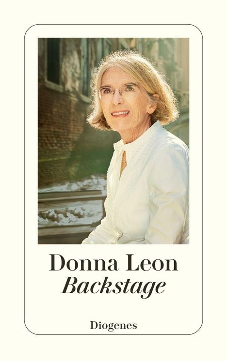 "Donna Leon, Backstage, Diogenes". Eine Frau mit grauem Haar und Brille trägt ein weißes Hemd und lächelt. Hintergrund: Stadt.