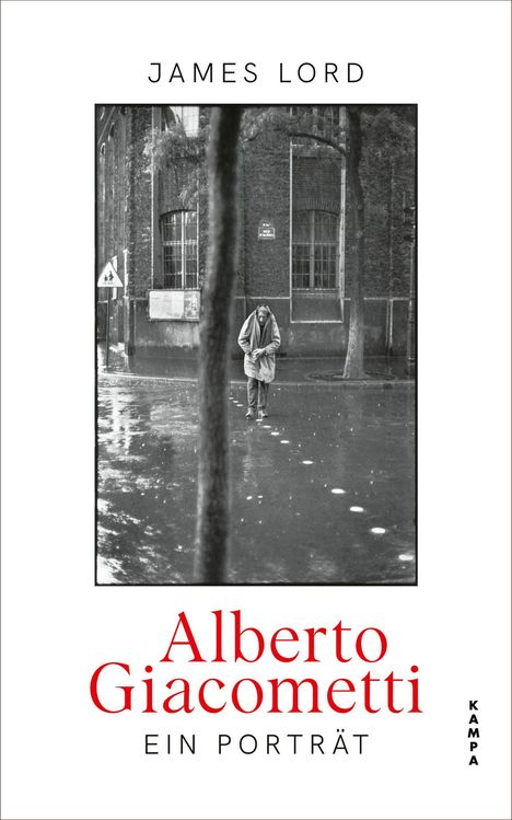 JAMES LORD. Alberto Giacometti: Ein Porträt. Schwarzweißfoto eines Mannes in nasser Straße vor Gebäude mit Bäumen.