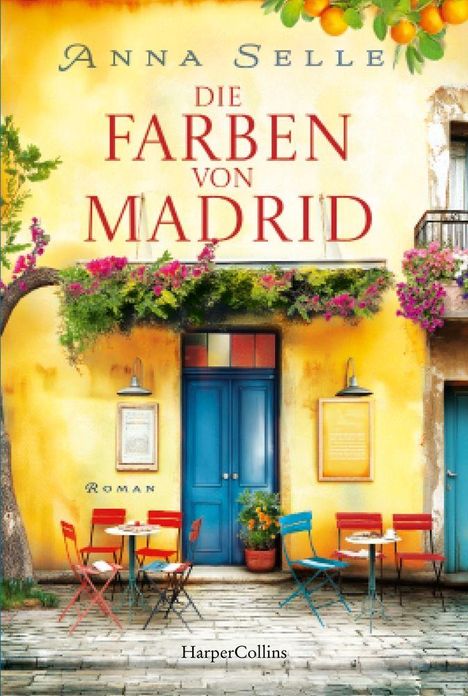 „Anna Selle, Die Farben von Madrid“. Bunte Fassade mit blauem Tür, Pflanzen und Café-Tischen in lebhaften Farben.