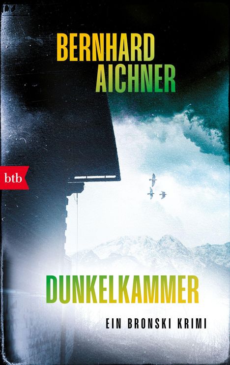 „BERNHARD AICHNER, DUNKELKAMMER, EIN BRONSKI KRIMI.“ Links ein rotes Logo „btb“, darunter Haus und Vögel vor Bergen.