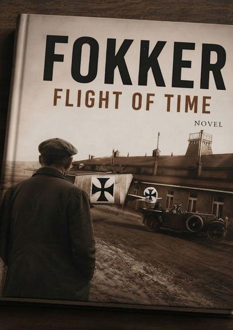 "FOKKER FLIGHT OF TIME NOVEL". Ein Mann blickt auf ein historisches Gebäude mit Flugzeugteilen und einem Auto.
