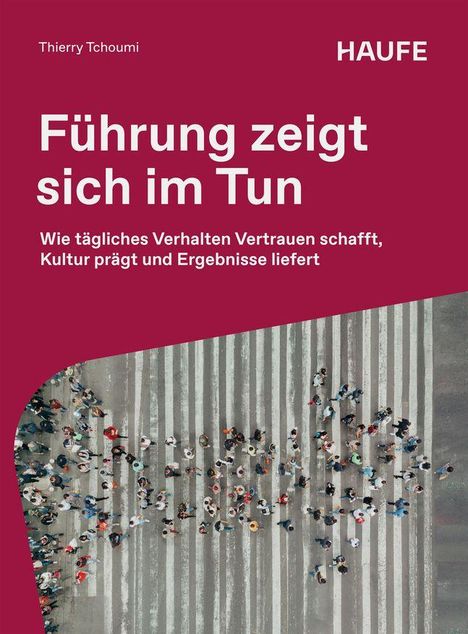 In großen weißen Buchstaben steht: "Führung zeigt sich im Tun". Unten sieht man Menschen, die einen Zebrastreifen überqueren.