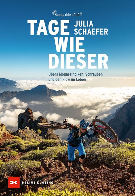 "Tage wie dieser" von Julia Schaefer: Ein Mountainbiker trägt sein Rad auf einem Berg mit Wolken im Hintergrund.