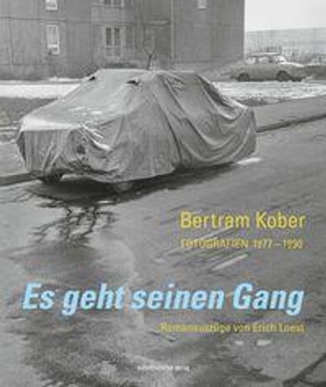 "Es geht seinen Gang" in Blau. "Bertram Kober Fotografien 1977-1990" in Gelb. Auto unter Plane auf grauer Straße.