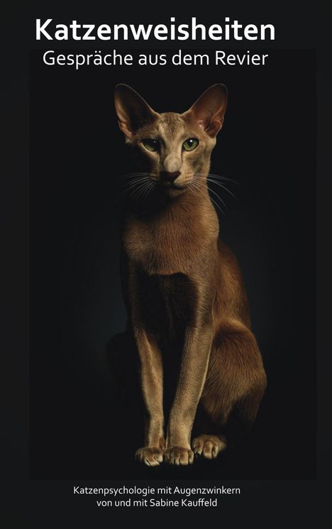 "Katzenweisheiten: Gespräche aus dem Revier. Katzenpsychologie mit Augenzwinkern von und mit Sabine Kauffeld." Eine Katze sitzt im Dunkeln.