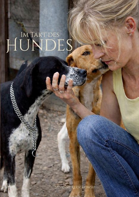 "Im Takt des Hundes" in großen Buchstaben. Eine Frau kniet zwischen zwei Hunden und berührt einen liebevoll.