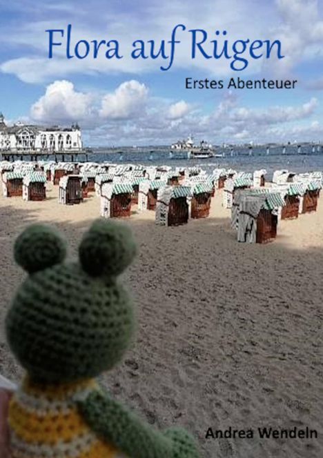 "Flora auf Rügen. Erstes Abenteuer. Andrea Wendeln." Strand mit Strandkörben und einer gestrickten Froschfigur im Vordergrund.