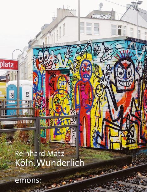 Reinhard Matz, Köln. Wunderlich, emons:. Bunt bemaltes Gebäude mit Graffiti-Figuren vor Häusern und Bahngleisen.