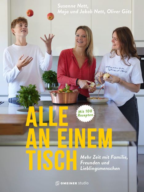 "Alle an einem Tisch", "Mit 100 Rezepten". Drei Menschen in einer Küche mit Obst und Kochtopf. Junge jongliert mit Äpfeln.