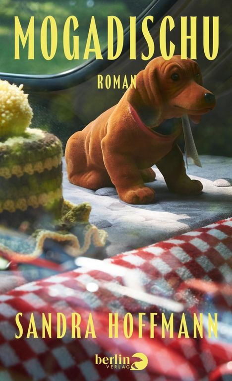 Text: "MOGADISCHU ROMAN", "SANDRA HOFFMANN". Ein kleines, braunes Stofftier auf einer karierten Decke.