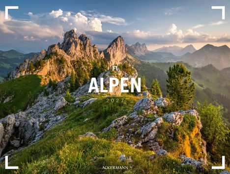 „ALPEN 2027“ steht im Vordergrund einer malerischen Berglandschaft mit felsigen Gipfeln und üppigem Grün im Abendlicht.