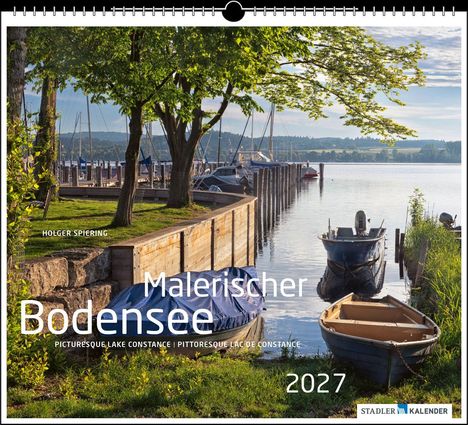 "MALERISCHER BODENSEE 2027" in großen Buchstaben. Boote am Steg, Bäume, ruhiges Wasser und Berge im Hintergrund. Kalender-Layout.