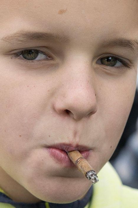 Ein Junge mit nachdenklichem Blick hält eine brennende Zigarette zwischen den Lippen.